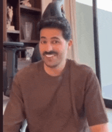 a man with a mustache is wearing a hat and smiling while sitting in a chair .