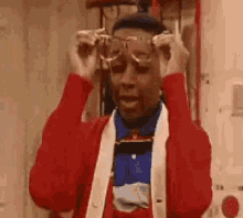 a man wearing a red sweater and a blue shirt is putting on glasses .