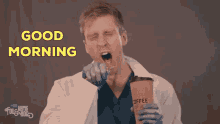 a man in a lab coat is yawning while holding a cup of coffee in his hand .