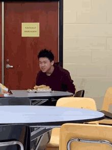a man is sitting at a table in a cafeteria with a plate of food on the table .