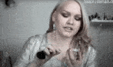 a woman in a silver top is applying makeup with a brush