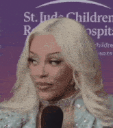 a woman with blonde hair is talking into a microphone in front of a st. jude children 's hospital sign