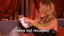 a woman is sitting on a couch holding a receipt and says receipt ( takes out receipts ) .
