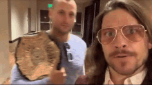 two men wearing sunglasses are standing next to each other and one of them is holding a wrestling belt