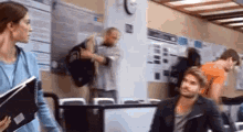 a man is sitting in front of a computer in a waiting room while a woman stands next to him .