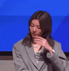 a woman in a suit is covering her face with her hand while standing in front of a blue screen .