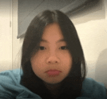 a young woman with long black hair is wearing a blue sweater and looking at the camera .