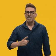 a man wearing glasses and a blue shirt is covering his face with his hands