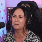 a woman wearing headphones and a leopard print shirt is crying while sitting in a gaming chair .