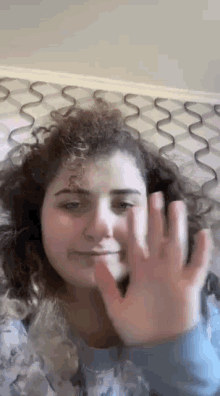 a woman with curly hair is holding her hand up in front of her face .