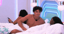 a shirtless man is laying on a bed next to two women