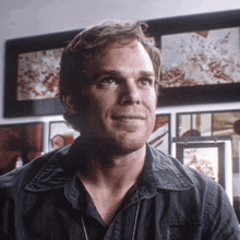 a man in a black shirt is smiling in front of a wall of framed pictures