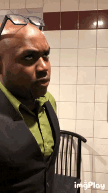 a man wearing glasses and a green shirt is standing in front of a white tiled wall ..