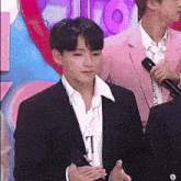 a man in a suit is talking into a microphone while standing next to another man in a pink suit .