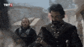 a man with a beard is holding a sword in front of a sign that says trt 1