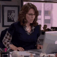 a woman is sitting at a desk working on a laptop computer .