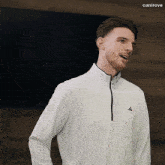 a man wearing a white adidas shirt stands in front of a wall