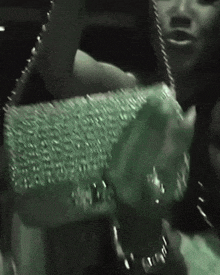 a woman is holding a green purse with rhinestones on the front