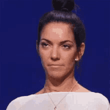 a woman with her eyes closed and her hair in a bun is wearing a white shirt and a necklace .