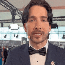 a man in a tuxedo and bow tie is talking into a microphone .