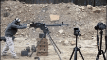 a man shooting a machine gun with a canon camera in the background
