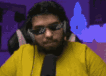 a man wearing headphones and sunglasses is sitting in front of a microphone in a room .