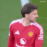 a man wearing a red adidas shirt is standing on a green field .