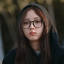 a woman wearing glasses and a black hoodie has a sad look on her face