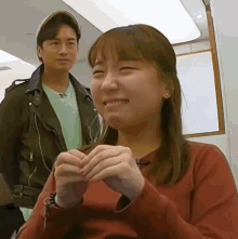 a man in a hat stands behind a woman in a red sweater