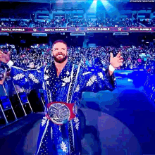 a man in a blue robe is standing in front of a crowd holding a championship belt .
