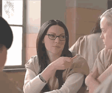 a woman wearing glasses is sitting at a table with a group of people .