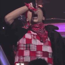 a man wearing a red bandana and a plaid shirt holds a microphone
