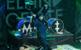 a man stands on a stage with a drum set that has the letter m on it