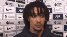 a man with dreadlocks is standing in front of a wall with advertisements for nike and axa