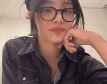 a woman wearing glasses and a denim shirt is looking at the camera