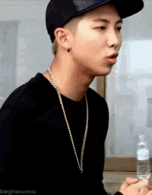 a man wearing a hat and a necklace is holding a bottle of water