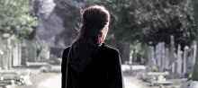 a woman in a black dress is walking down a cemetery .