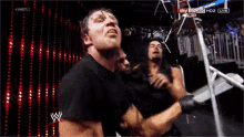 a group of wrestlers are standing in a ring and one of them is wearing a black shirt with the letter w on it