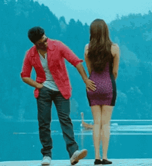 a man in a pink jacket is touching a woman 's butt while standing next to a body of water .