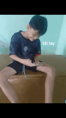 a young boy is sitting on a bench looking at a cell phone with a caption that says tất tay