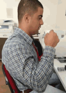 a man in a plaid shirt is sitting at a desk with his fist up
