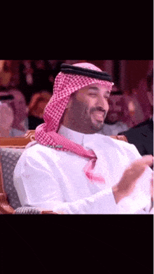 a man wearing a head scarf and a white shirt is sitting in a chair