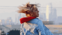 a woman wearing a red hoodie and a denim jacket is running in front of a city .