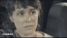 a woman is sitting in the back seat of a car looking at the camera with a sad look on her face .