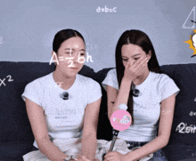 two women are sitting on a couch and one of them is wearing a shirt that says denial