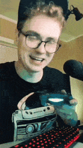 a man wearing glasses is holding a video game controller in front of a microphone
