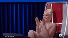 a woman in a white dress is sitting in a red chair applauding .
