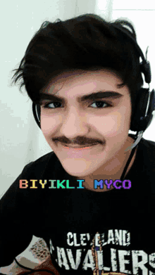 a young man with a mustache wearing headphones and a cleveland cavaliers shirt