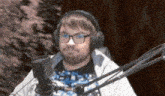 a man wearing headphones and glasses sitting in front of a microphone .