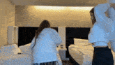 two women are having a pillow fight in a hotel room with two beds .